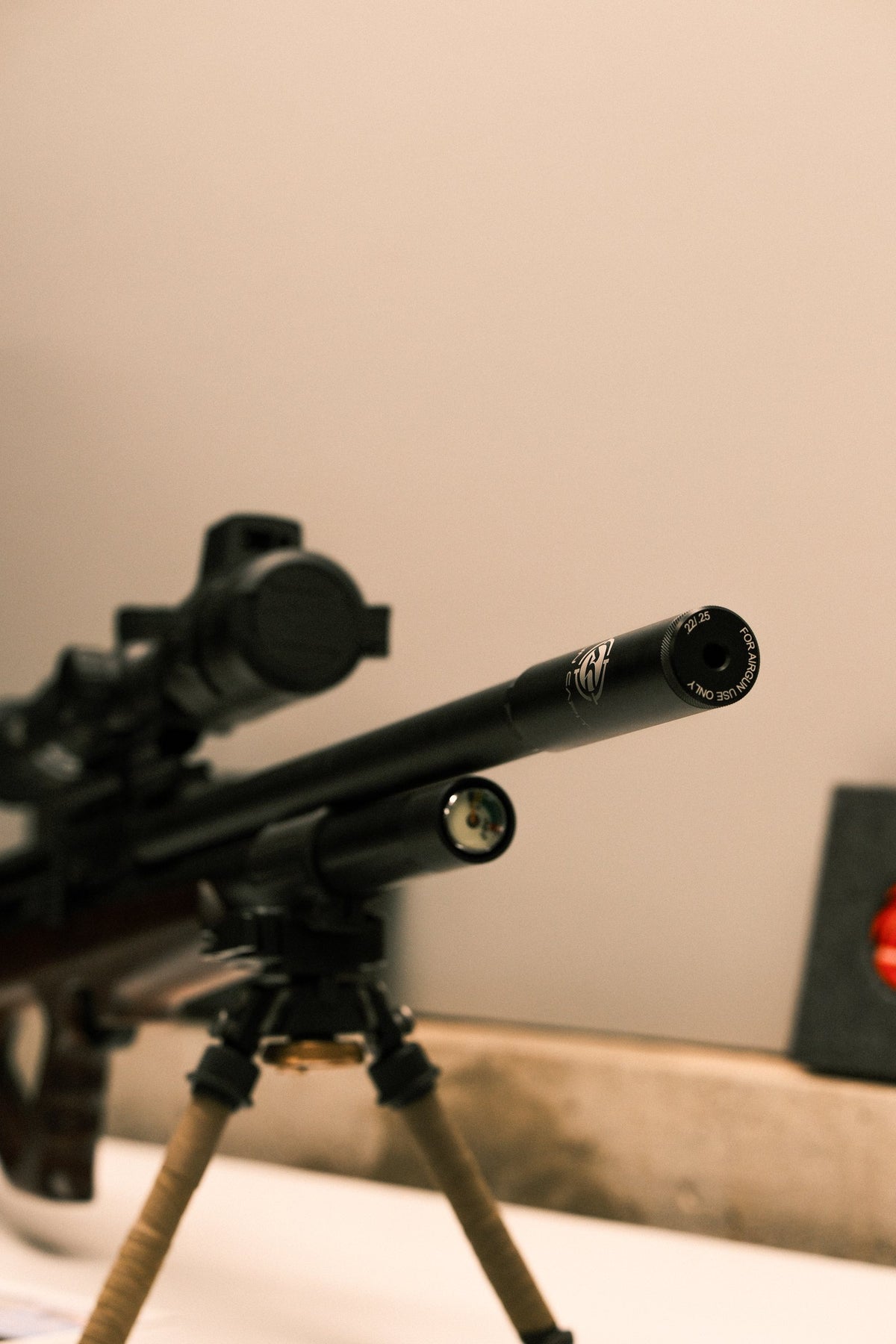 Air rifle on a bipod with an Airgun Capital suppressor, on an indoor bench