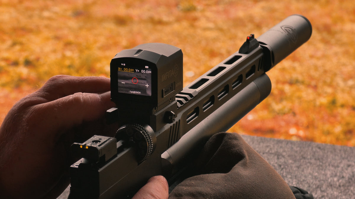 Hands holding a suppressed air pistol with a digital sight at the range