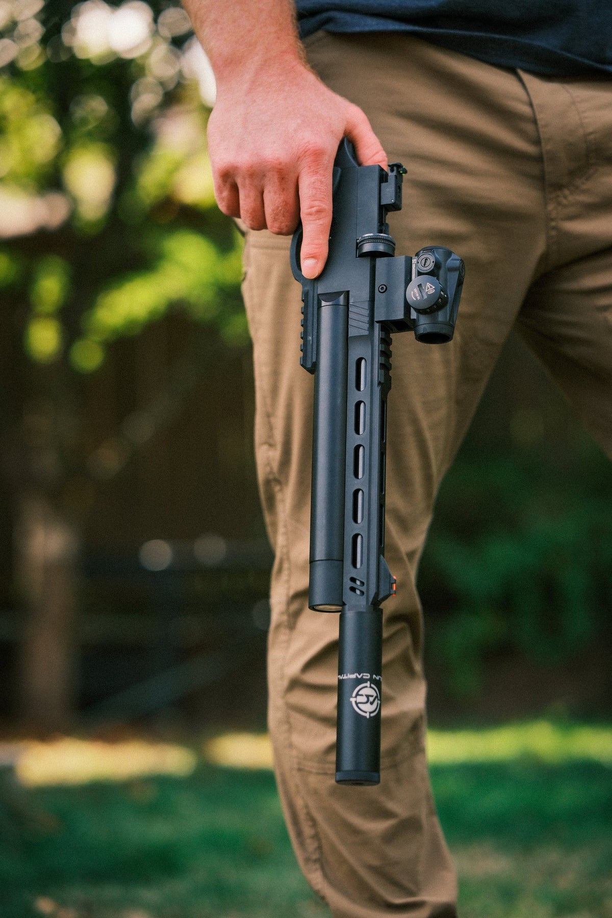 Shooter carrying an air pistol with a long suppressor and red dot